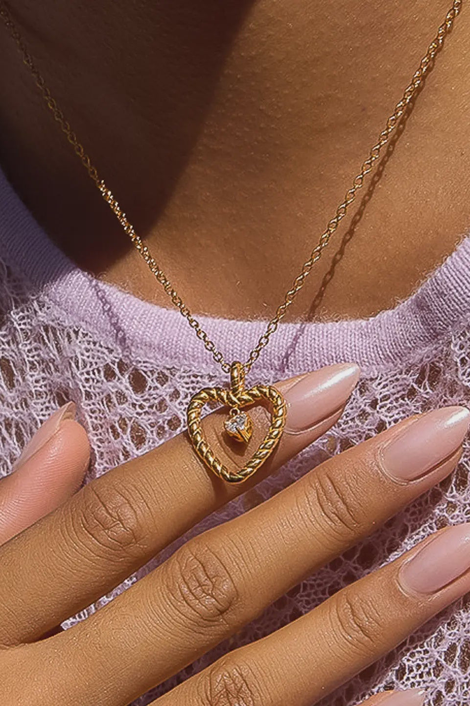 Gold necklace with a heart-shaped pendant worn by a person against a pink lace background