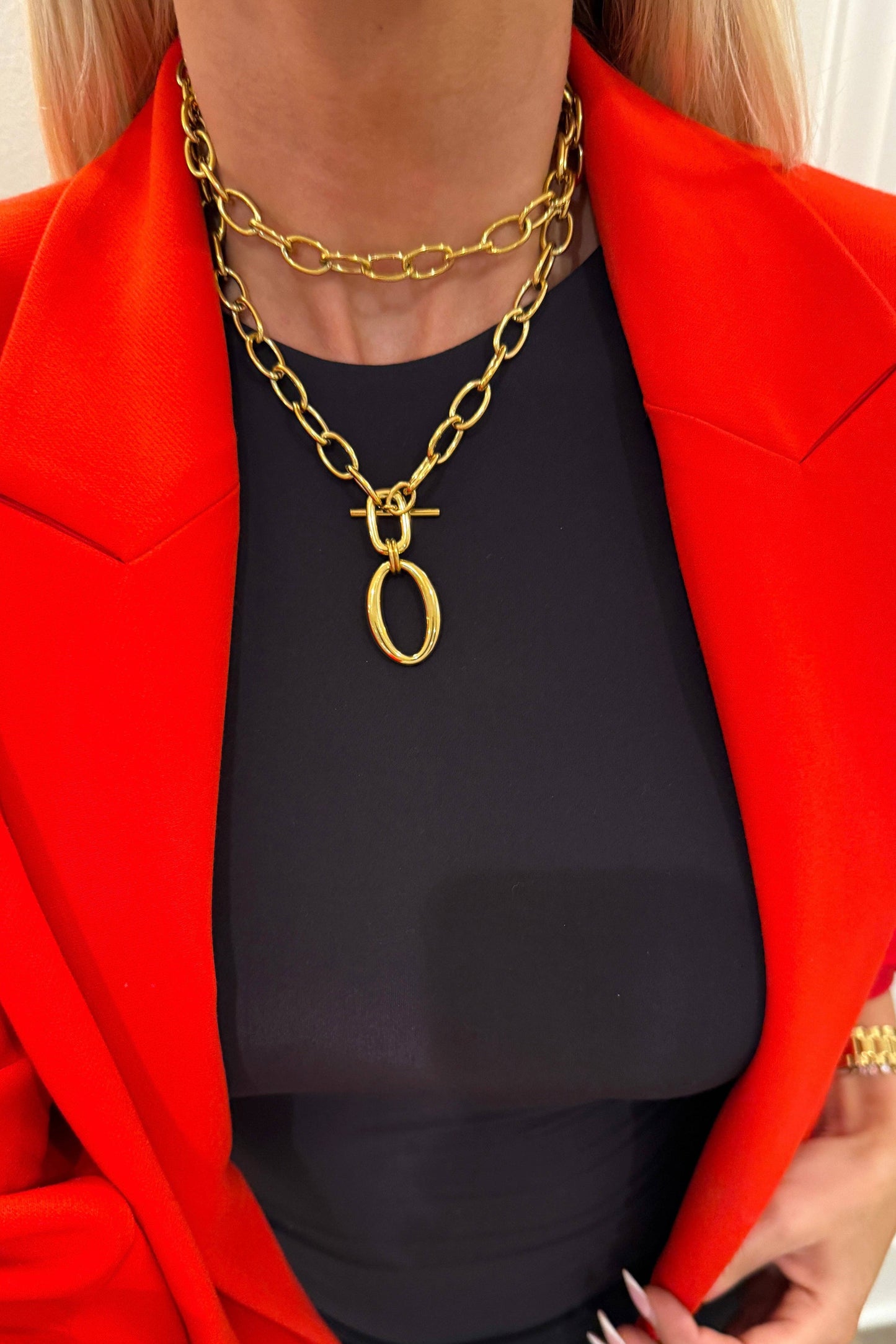 Person wearing a red blazer and black top with a gold chain necklace.