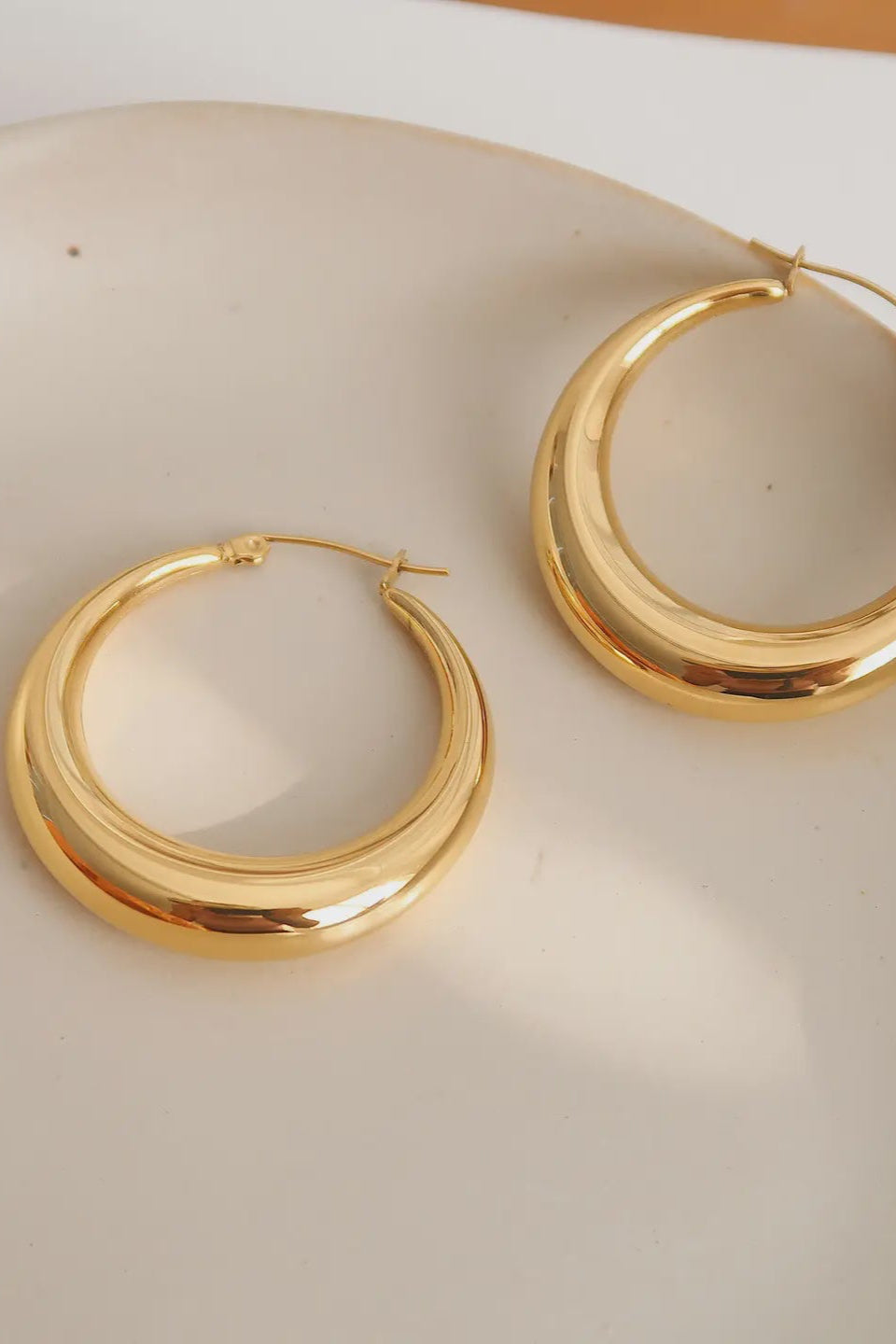 Gold hoop earrings on a beige surface
