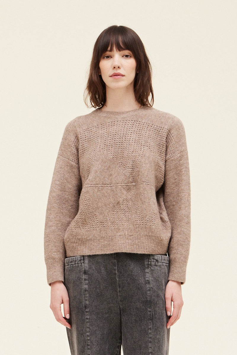 Woman wearing a brown knitted sweater and dark jeans on a beige background