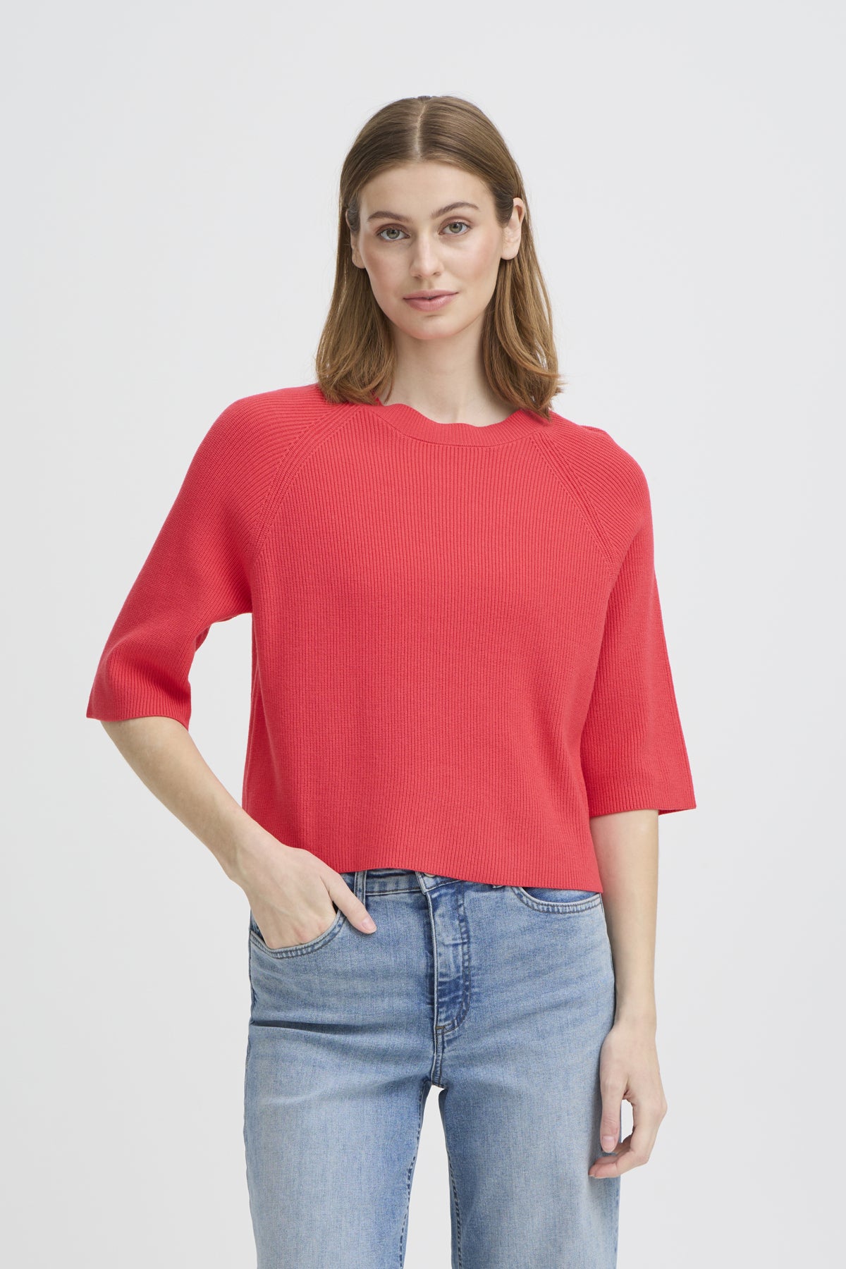 Woman wearing a red sweater and blue jeans on a light gray background