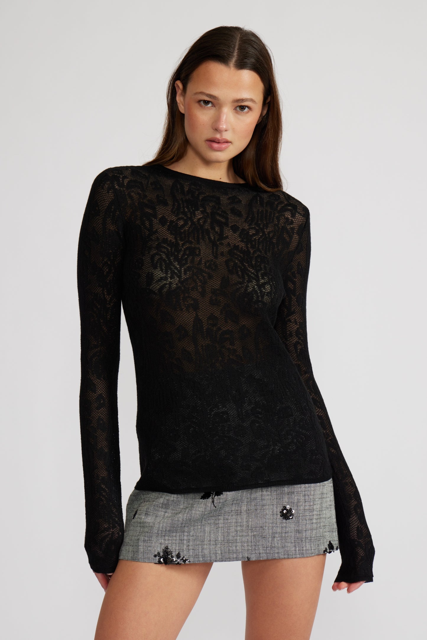 Woman wearing a black lace top and gray skirt on a white background