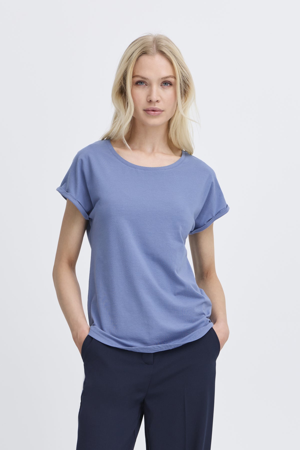 Woman wearing a blue t-shirt and dark pants on a light gray background