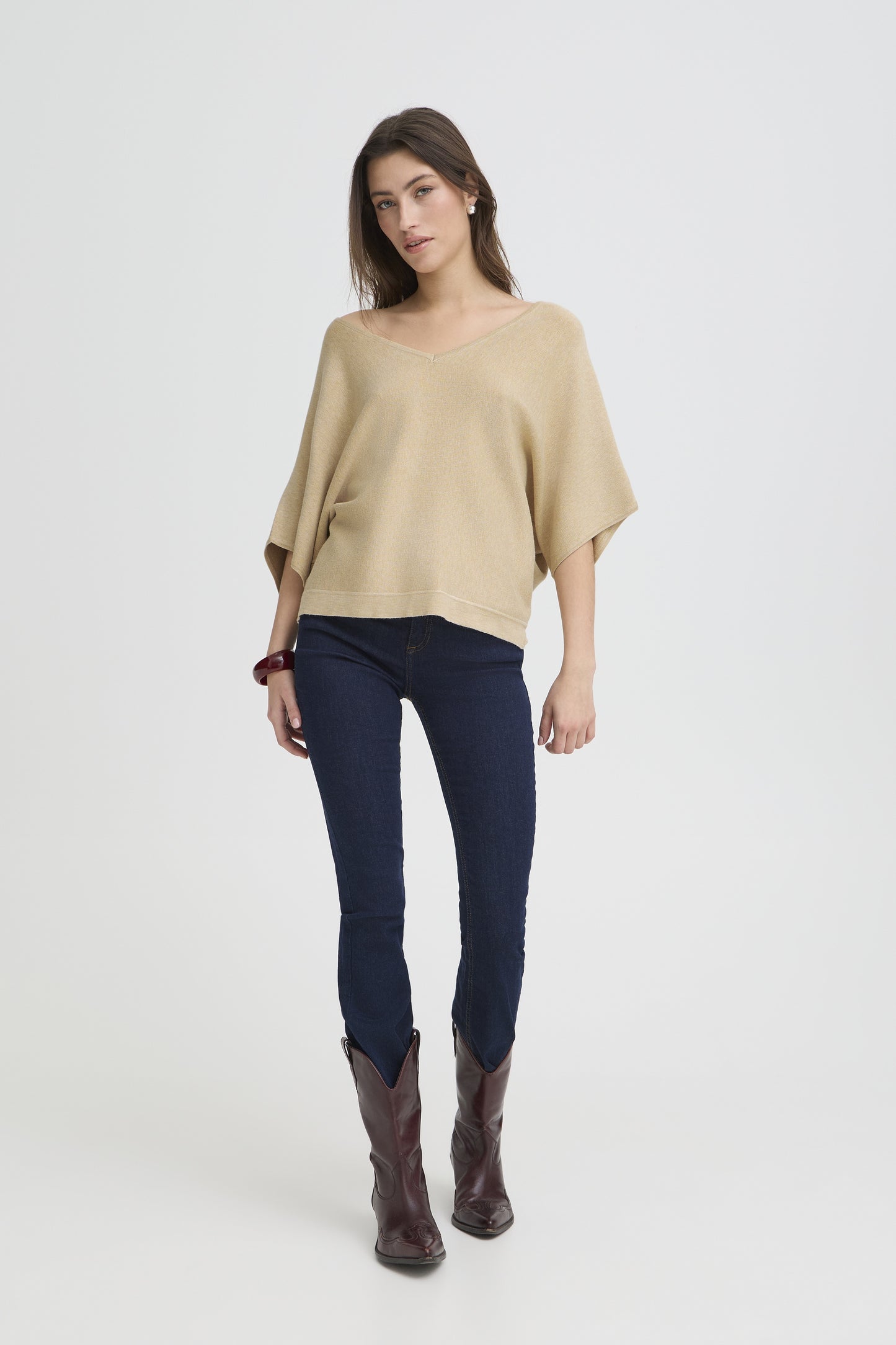 Woman wearing a beige sweater, navy pants, and brown boots on a white background