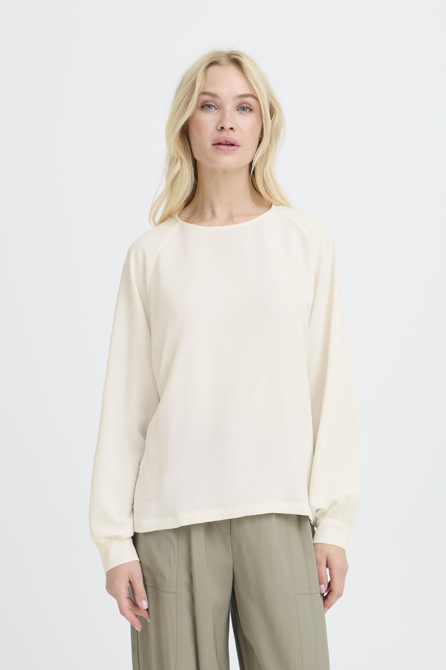 Woman wearing a cream-colored sweater and beige pants on a white background