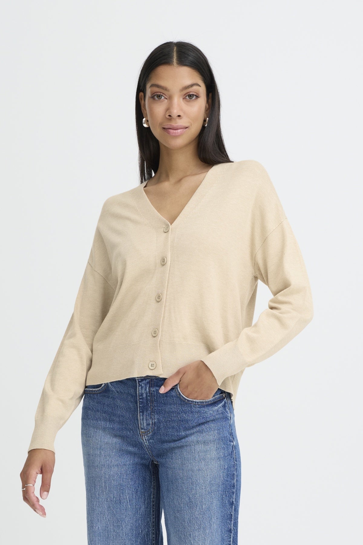 Woman wearing a beige cardigan and blue jeans on a white background