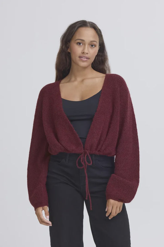 Woman wearing a burgundy cardigan over a black top and pants on a light gray background