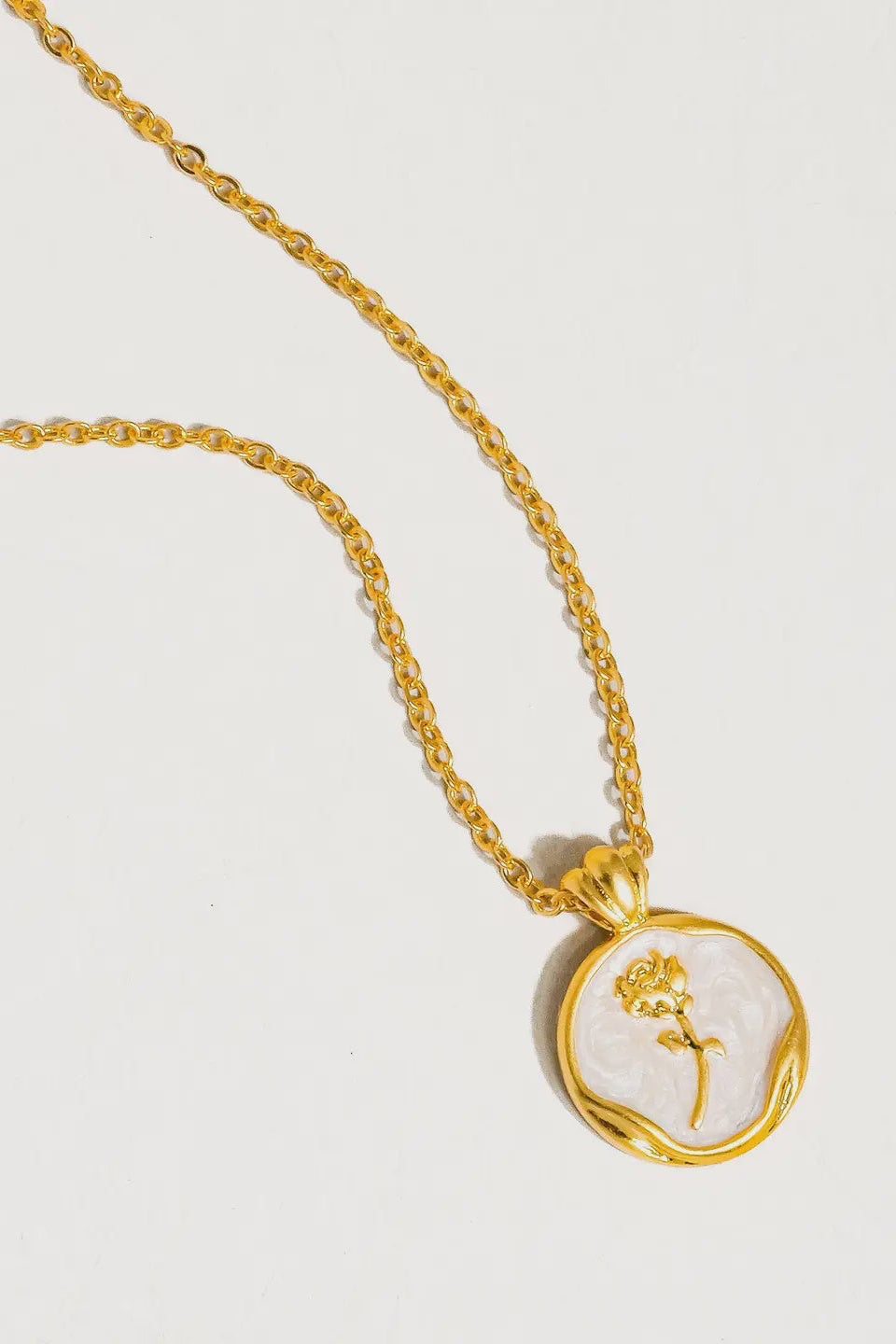 Gold necklace with a pendant featuring a floral design on a light gray background