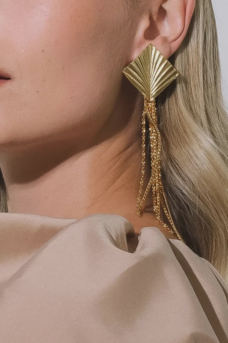 Close-up of a woman wearing gold earrings with tassels against a neutral background