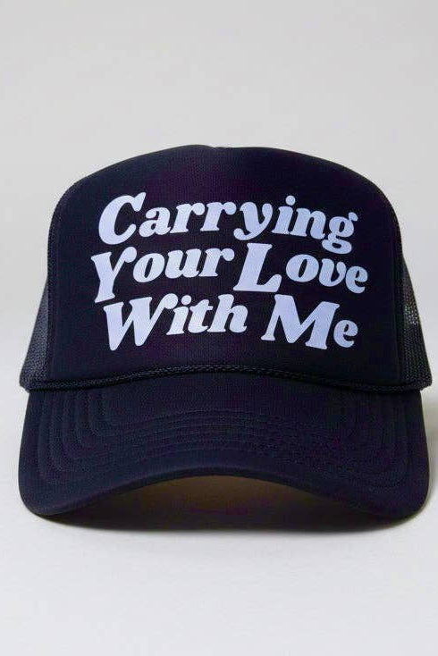 A navy blue trucker hat with white embroidered text reading 'Carrying Your Love With Me' on the front panel, set against a plain light gray background.