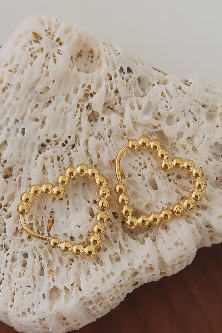 Gold heart-shaped earrings on a textured white stone surface