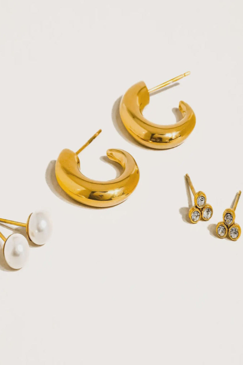 Set of gold hoop earrings and pearl-studded earrings on a light background