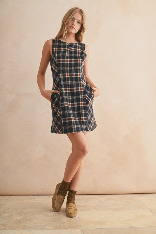 Woman wearing a plaid dress standing against a beige wall.