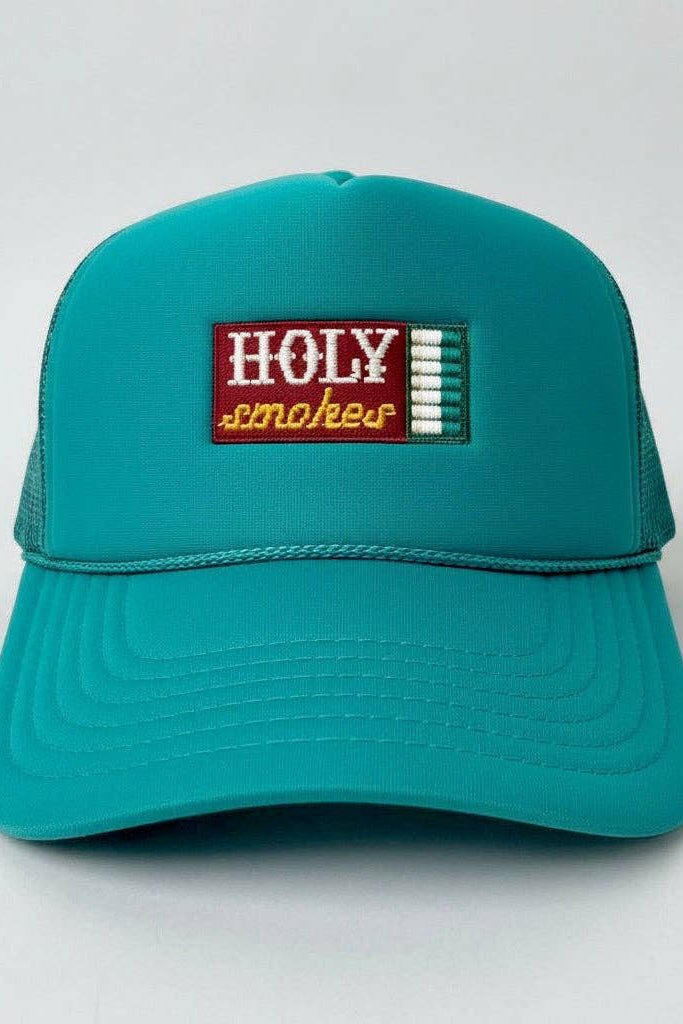 A teal trucker hat with a rectangular embroidered patch on the front that reads 'HOLY smokes' in white and yellow, set against a plain light gray background.