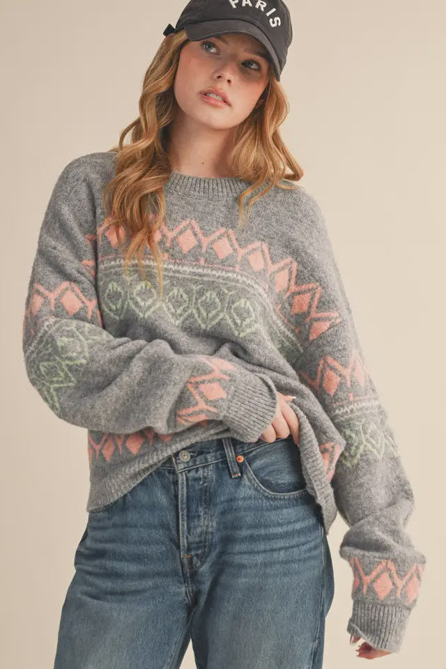 Person wearing a gray sweater with geometric patterns and blue jeans on a beige background