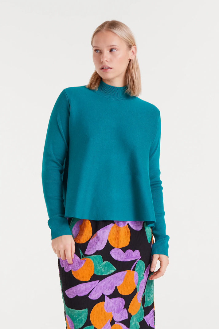 Woman wearing a teal sweater and colorful skirt on a white background