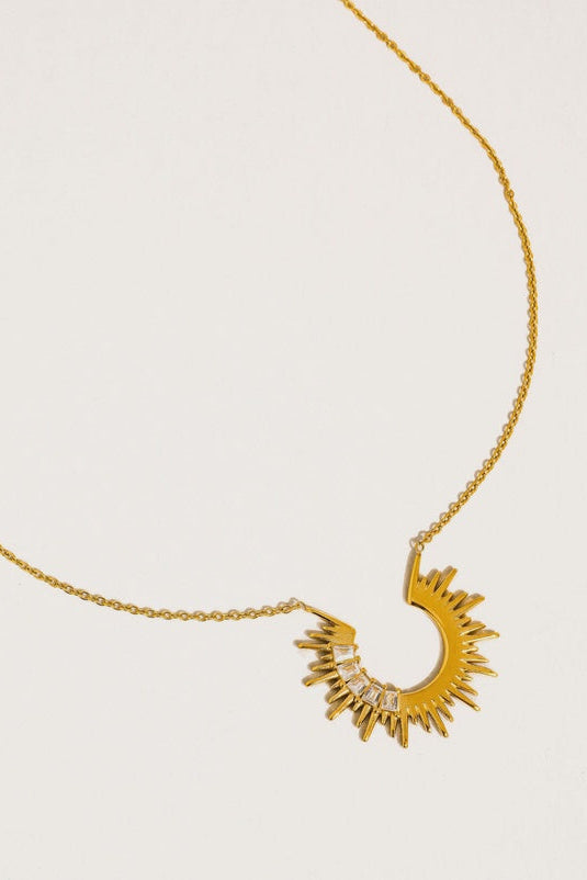 Gold necklace with a sun-shaped pendant on a light beige background
