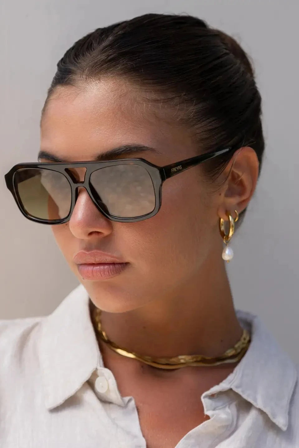 Woman wearing sunglasses and a white shirt with a neutral background