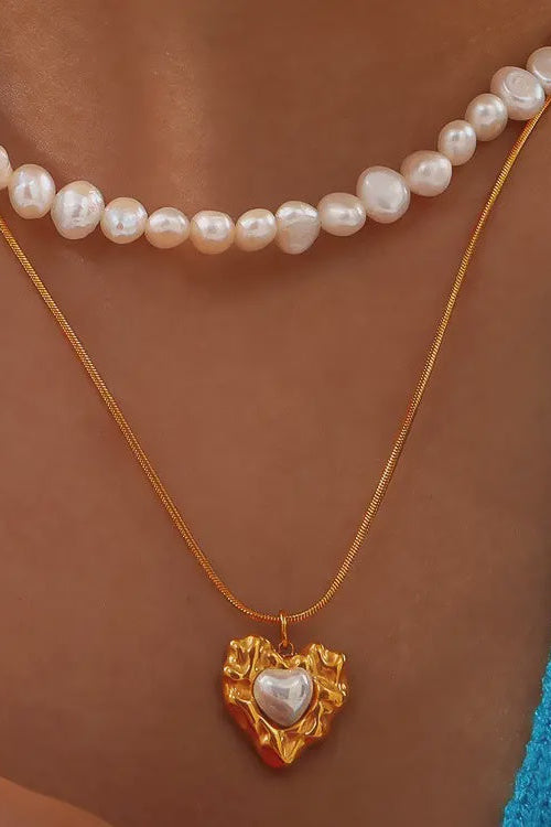 Gold necklace with a heart-shaped pendant worn by a person against a blue fabric background