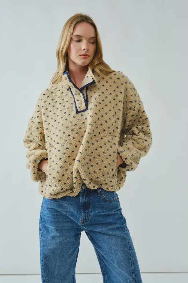 Woman wearing a beige patterned pullover with blue jeans against a light gray background