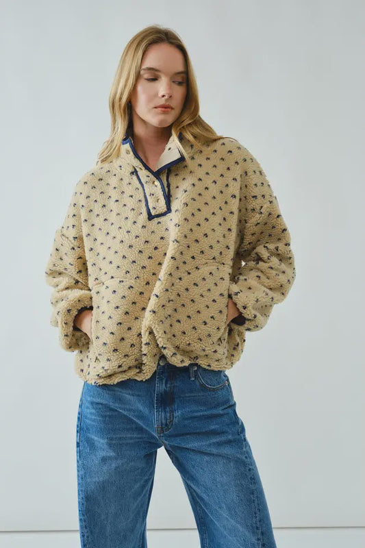 Woman wearing a beige patterned pullover with blue jeans against a light gray background