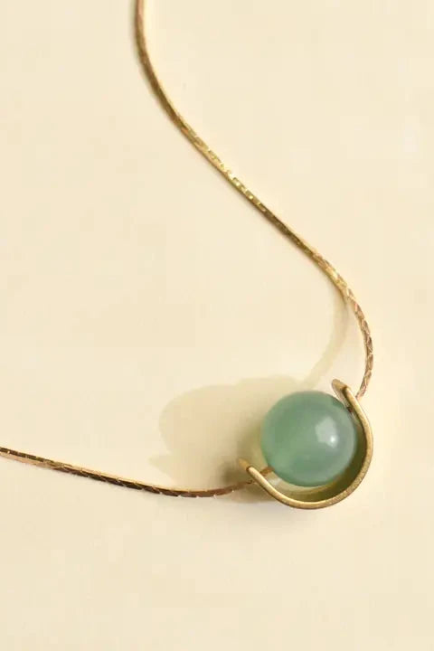 Gold necklace with a green gemstone on a beige background
