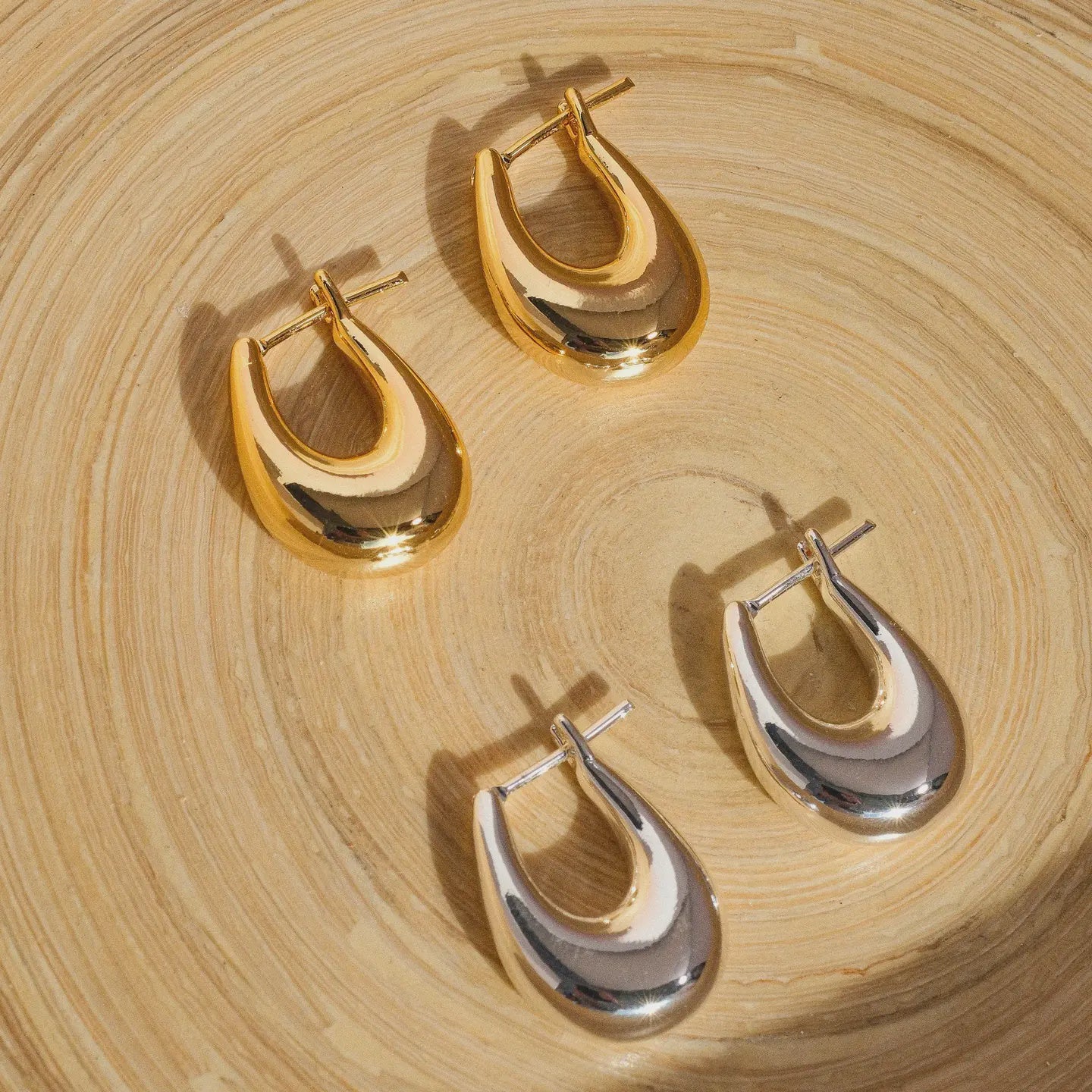 Two pairs of gold and silver hoop earrings on a wooden surface