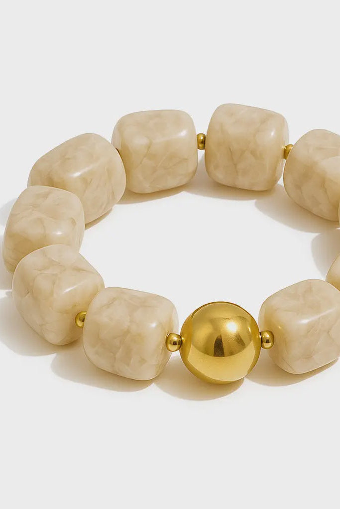Beige beaded bracelet with a gold ball on a light gray background