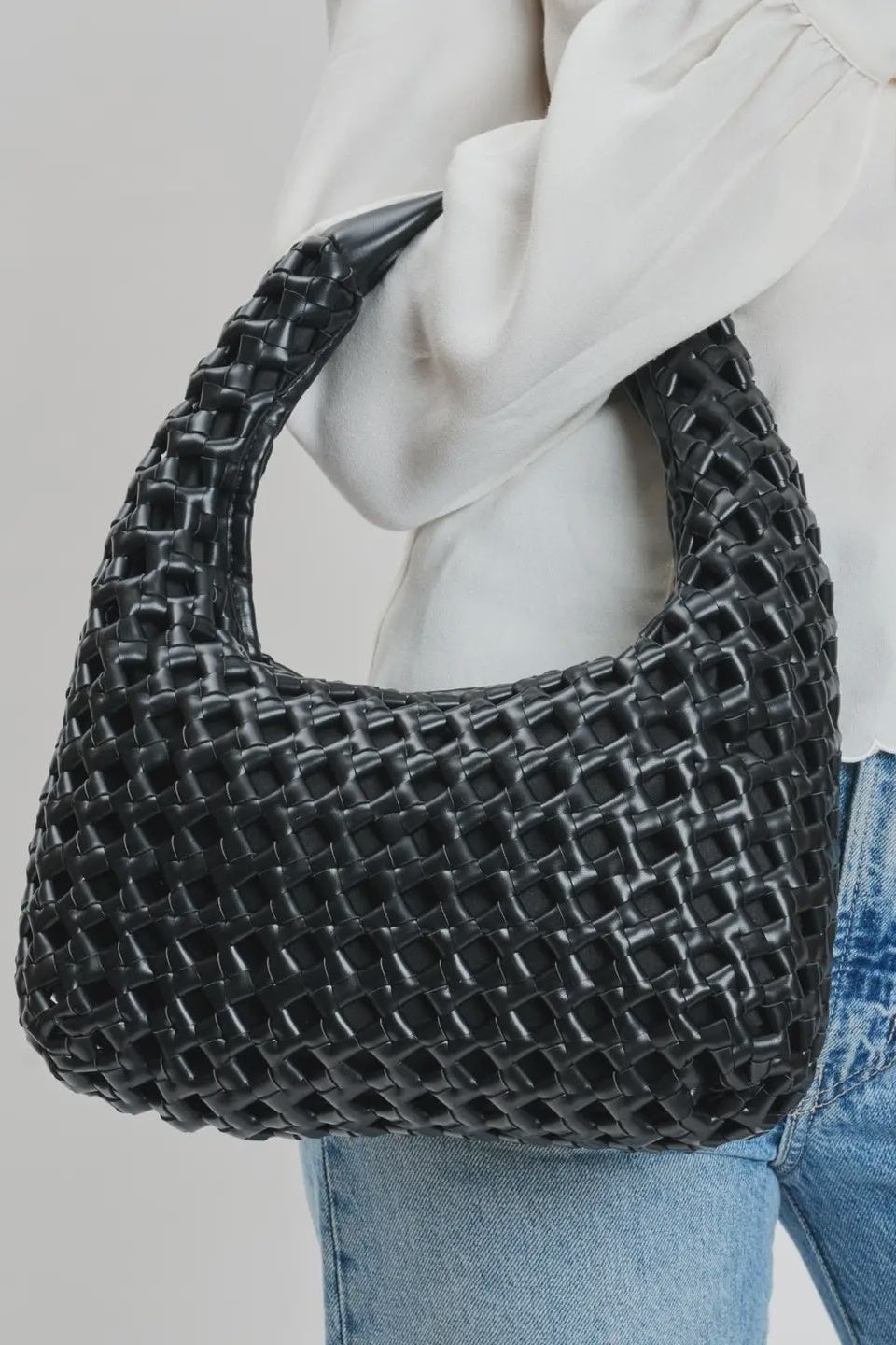Person holding a black woven handbag against a neutral background