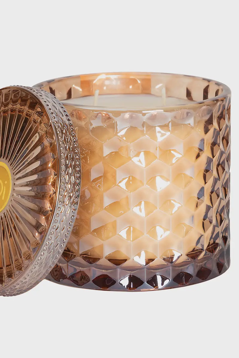 A 15oz shimmer candle with a hazelnut macchiato scent, encased in a dark amber glass with a geometric pattern.