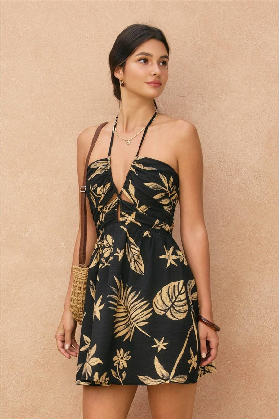 Woman wearing a black dress with gold floral pattern against a beige background