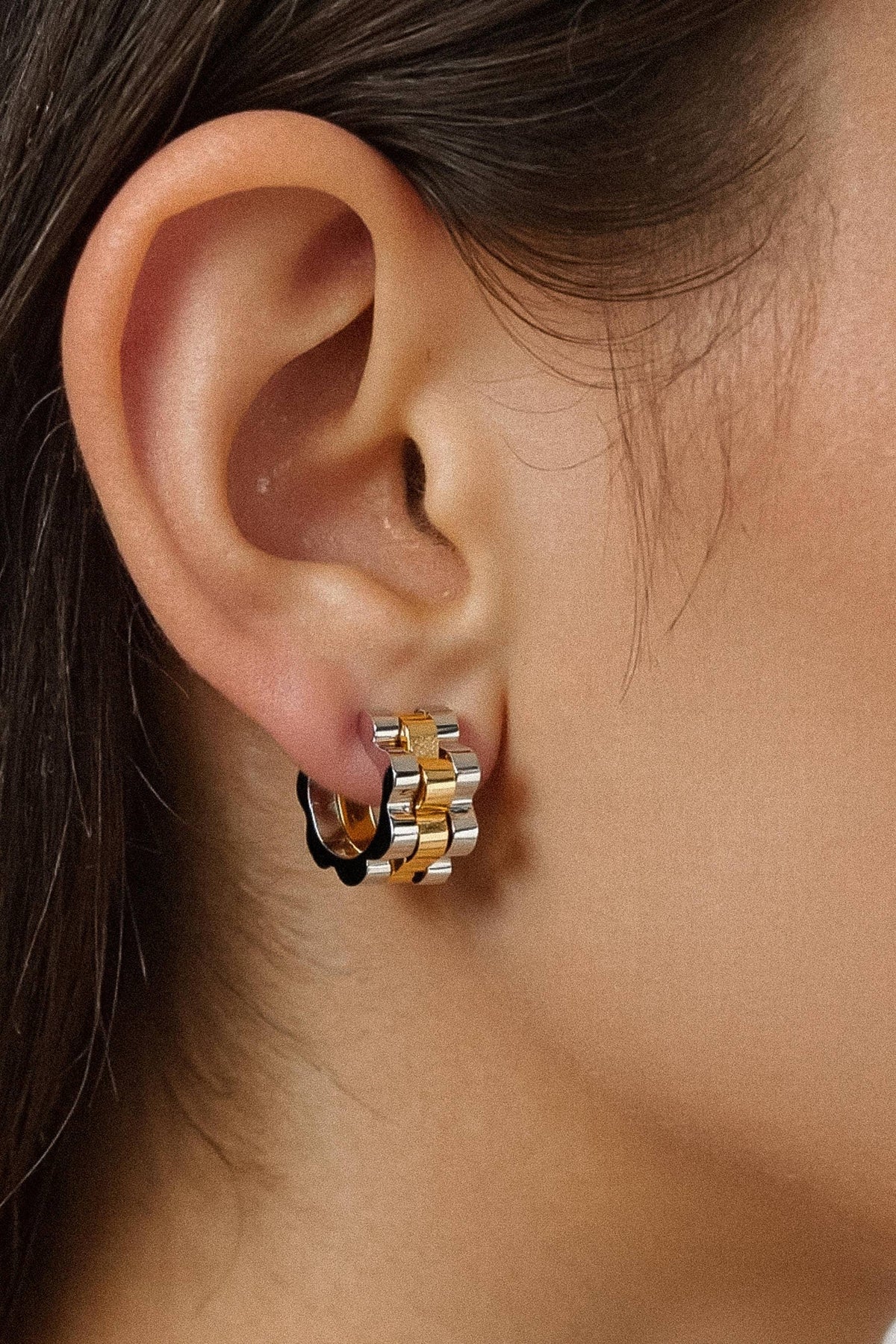 A close-up of a person's ear wearing a small hoop earring with a two-tone gold and silver chain design and a black accent.