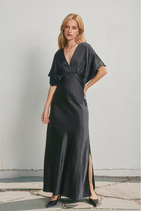 Woman wearing a black evening gown with a slit on a light gray background