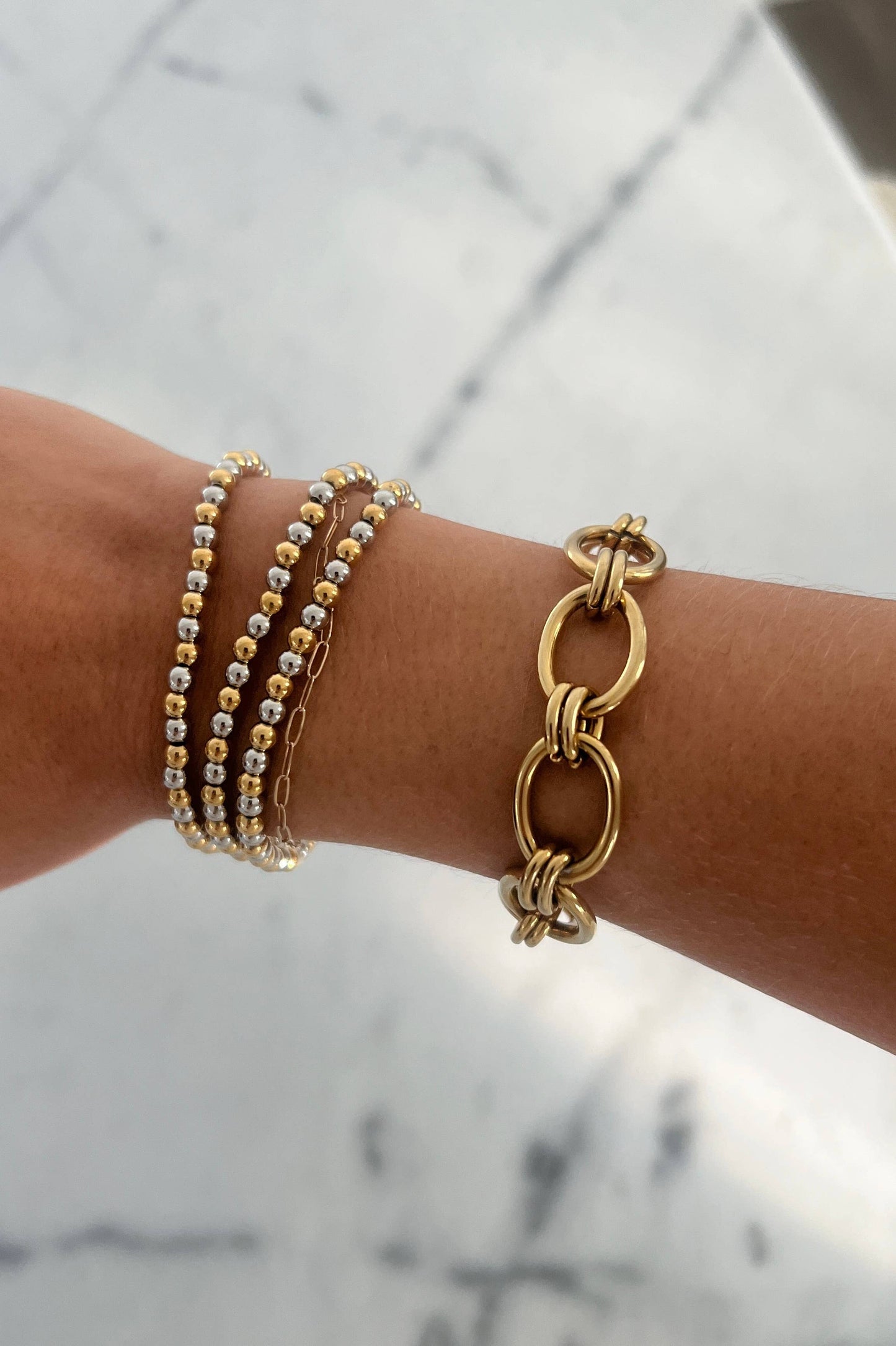 Gold bracelets on a wrist with a marble background