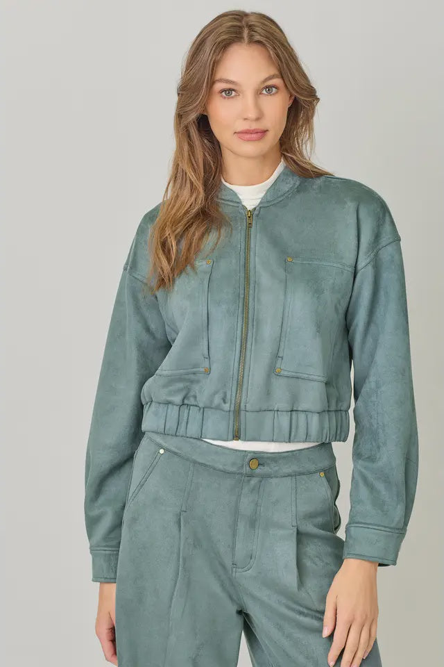 Woman wearing a teal jacket and pants on a plain background