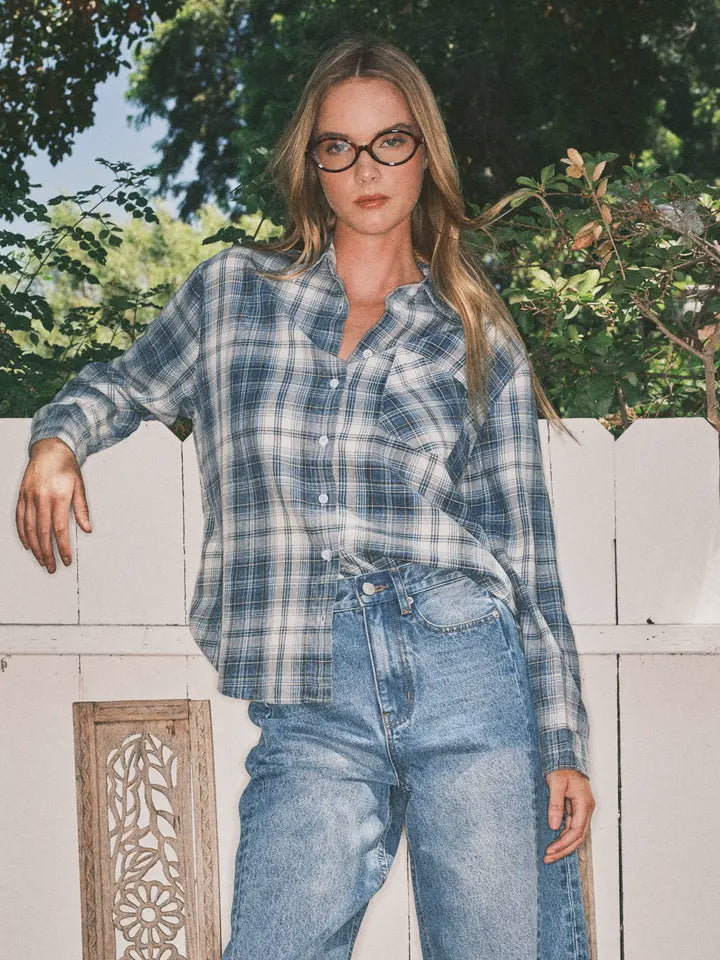 Woman wearing a plaid shirt and jeans outdoors with greenery in the background