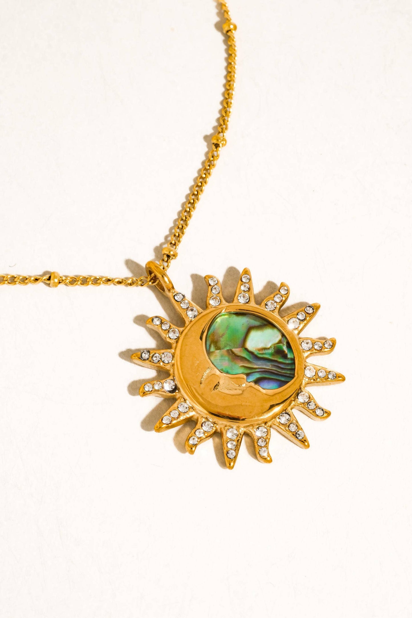 Gold necklace with a sun design and green stone on a white background