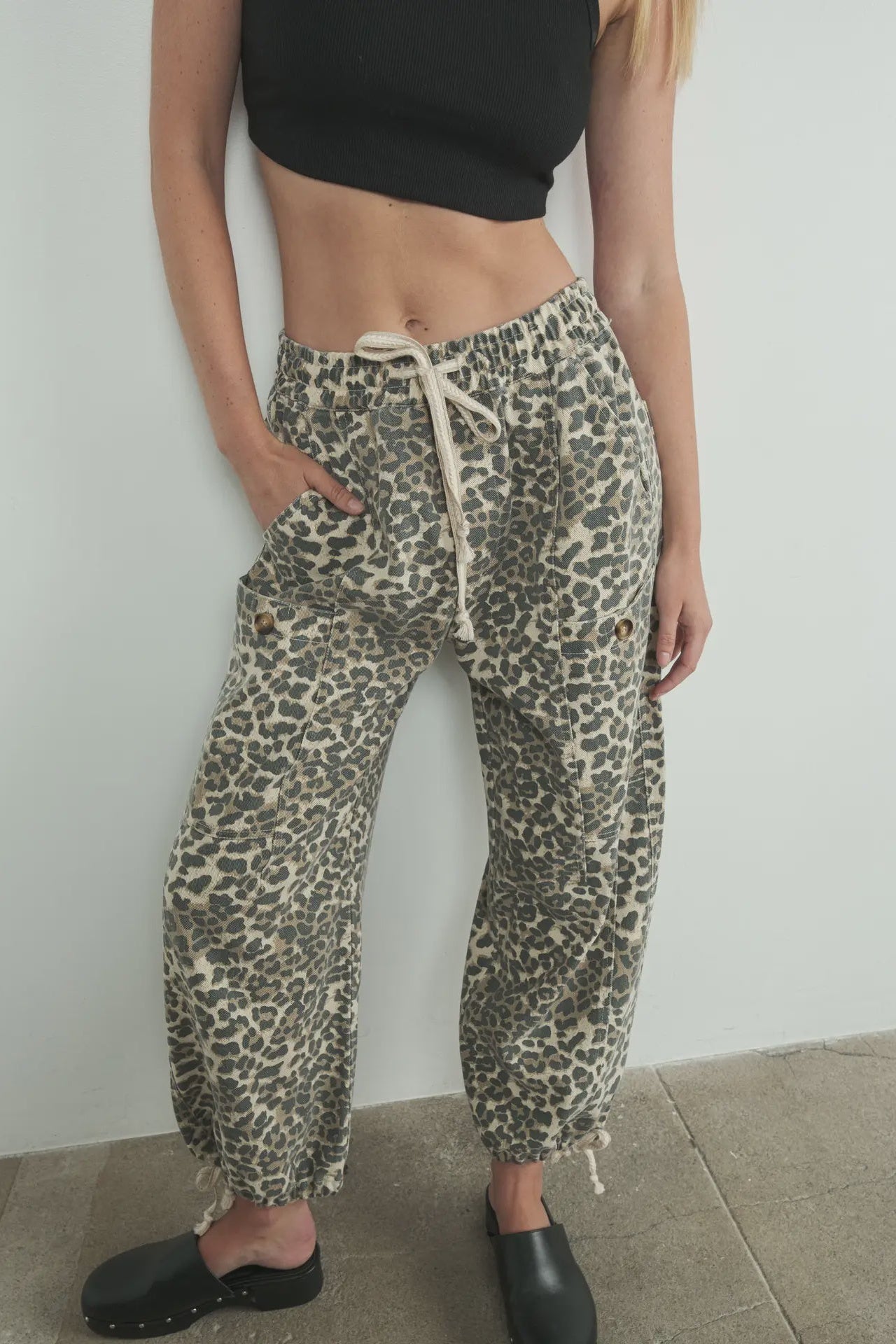 Person wearing leopard print pants and black shoes against a plain background