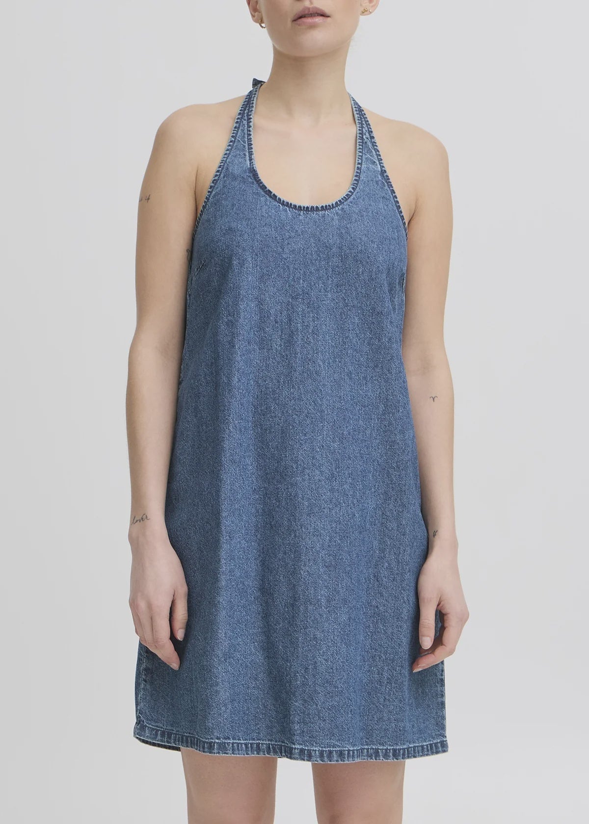 Stock photo shows a model wearing a denim halter mini dress