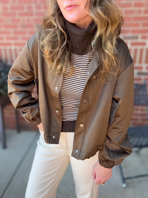 Person wearing a brown jacket over a striped shirt with a brick wall background