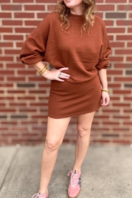 Person wearing a brown dress and pink sneakers in front of a brick wall