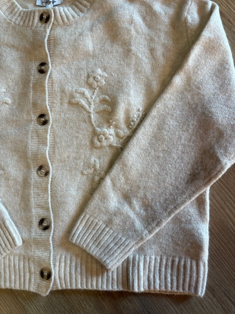 Beige cardigan with floral embroidery on a wooden surface
