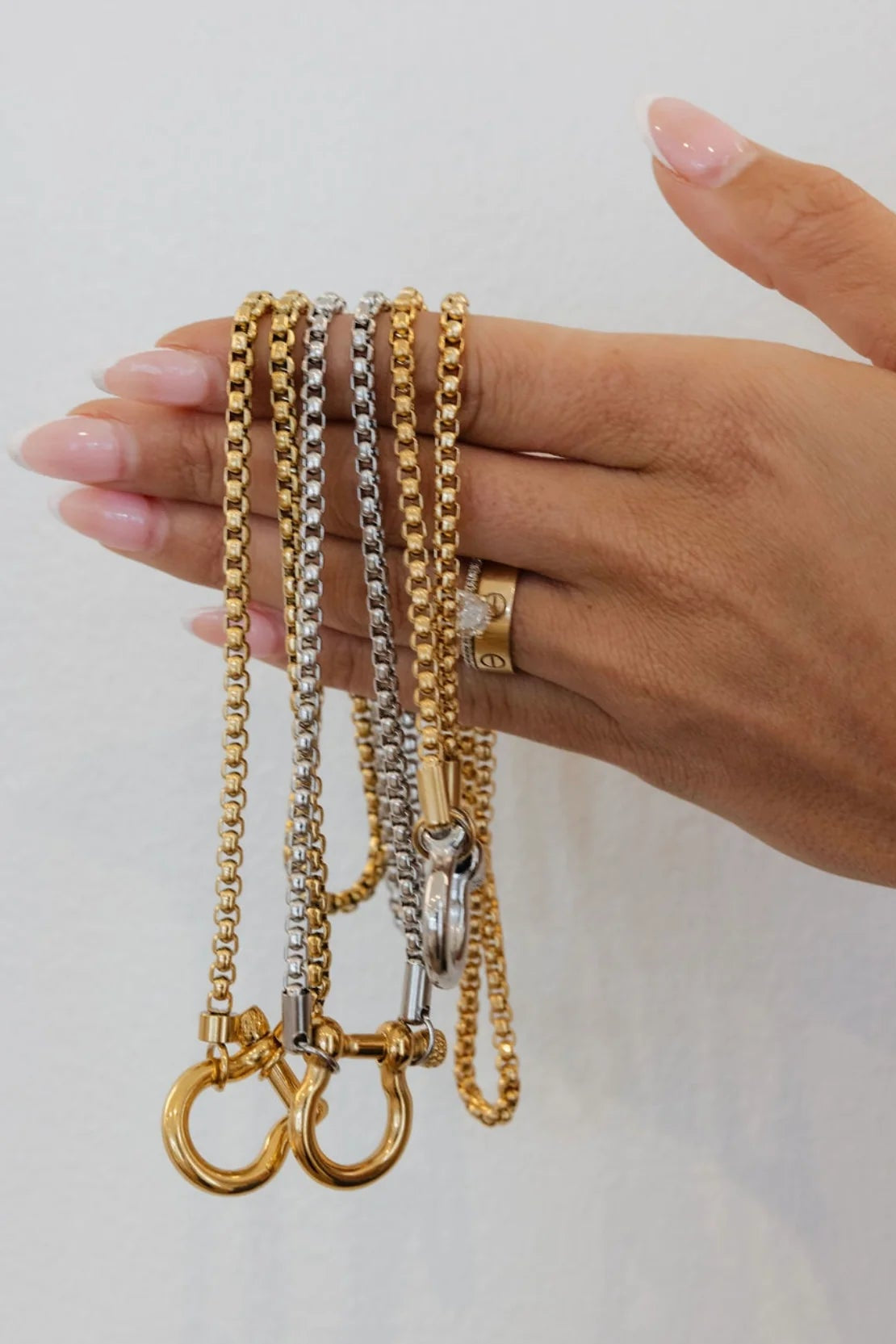 Hand holding three gold and silver chains against a light background