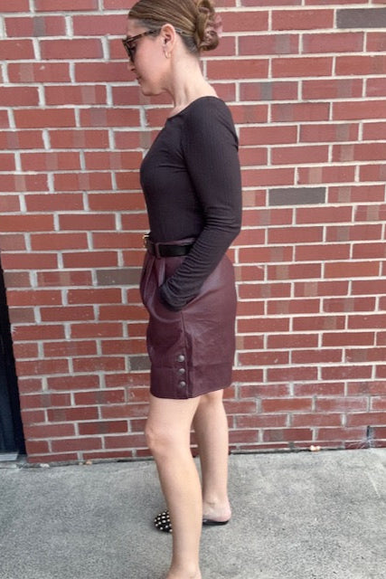 Person wearing a dark coat and maroon dress on a red brick sidewalk.