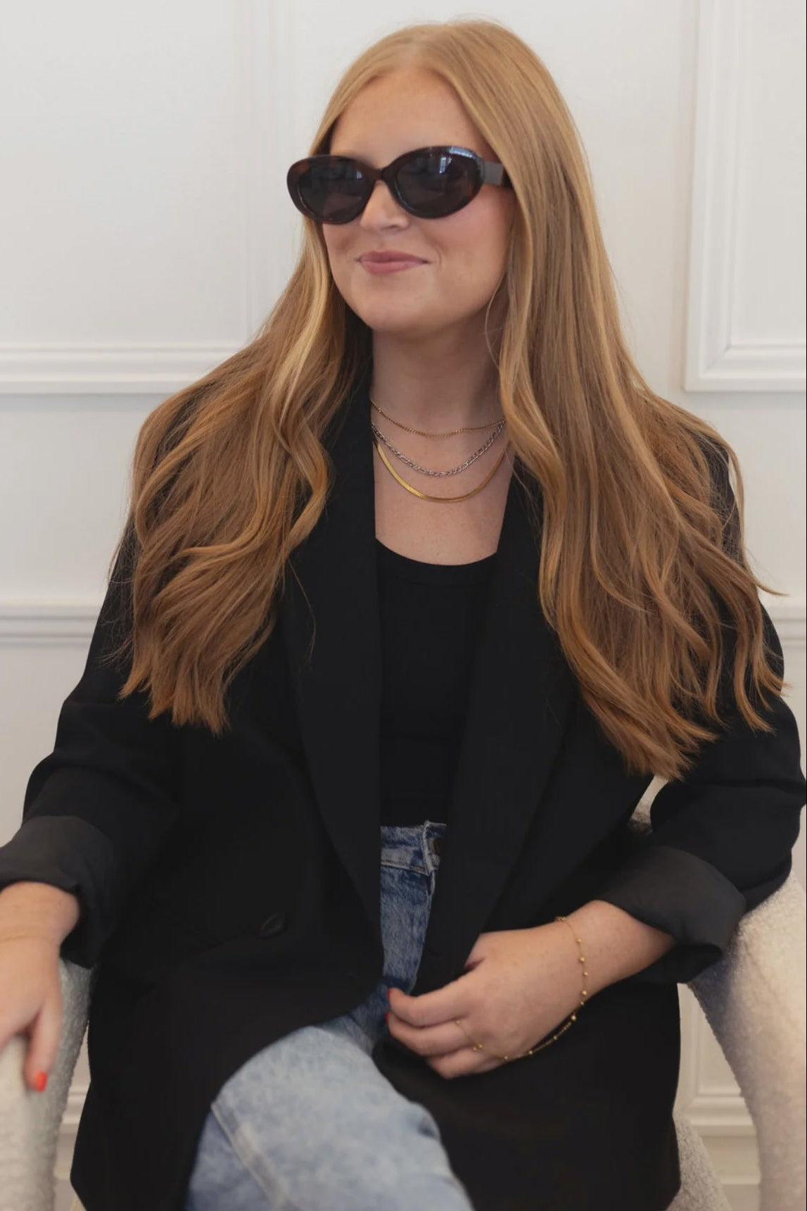 Woman wearing sunglasses and a black outfit sitting on a white chair.