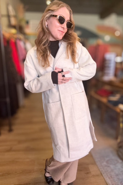 Person wearing a white coat and sunglasses in an indoor setting with blurred background