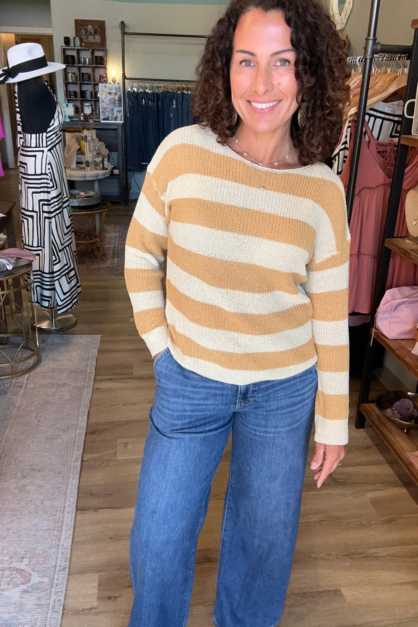 Woman wearing a striped sweater and jeans standing in a room with furniture and decor.