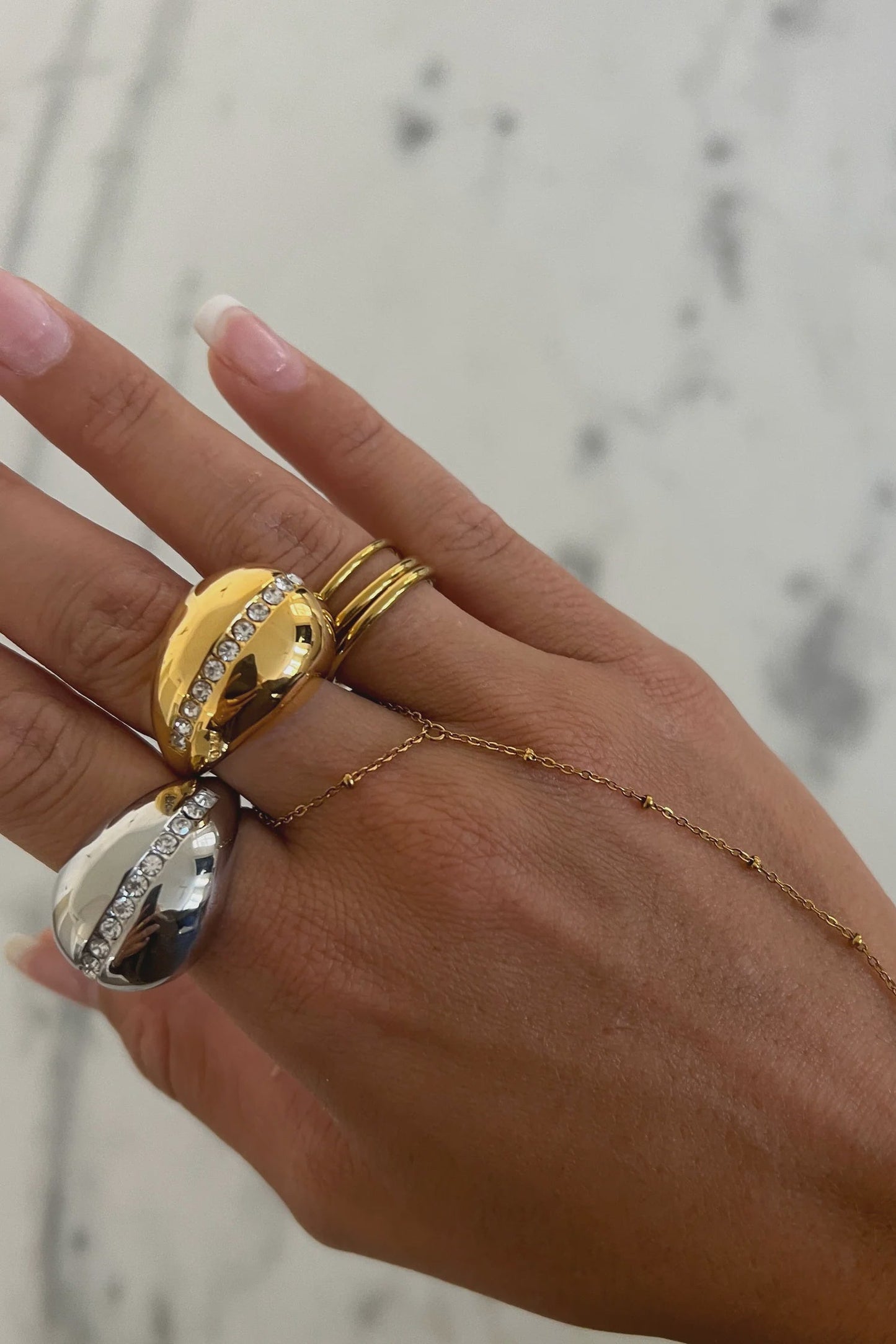 Hand wearing gold rings with a blurred marble background