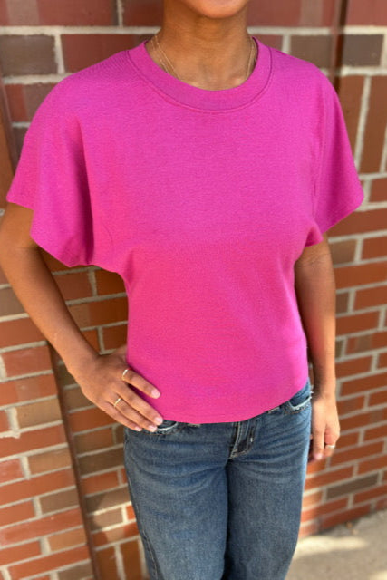 Person wearing a bright pink t-shirt and blue jeans standing against a brick wall.