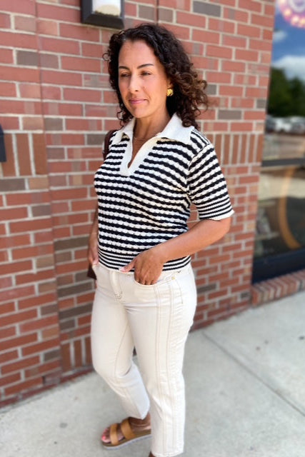 Woman wearing a black and white striped shirt and white pants standing in front of a brick wall.